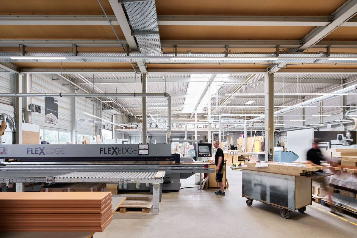 Produktionshalle von Messeprojekt in Leipzig mit FLEXEDGE-Kantenbearbeitung, Holzplatten und Mitarbeitern bei der Fertigung von Messeständen